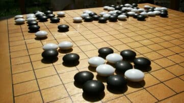 Black and white pieces on a Chinese Go board, by Donarreiskoffer